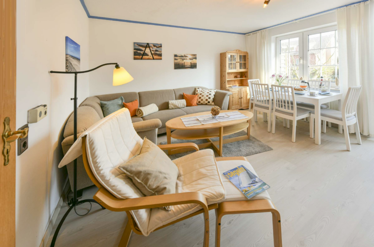 Heller Wohn- und Essbereich mit Sofa, Esstisch, großen Fenstern und Zugang zur Terrasse in einer gemütlichen Ferienwohnung.
