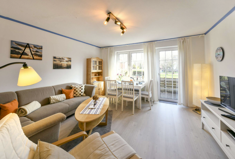 Gemütlicher Wohnbereich mit Ecksofa, Relaxsessel, Esstisch und großen Fenstern in einer modernen Ferienwohnung.